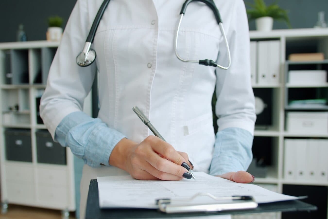 Profesional de la salud con ambo escribe en una planilla apoyada sobre una carpeta.